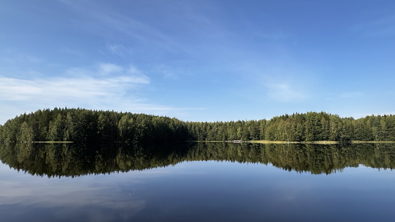 Saari tyynellä järvellä. Saarella on paljon puustoa. Järvi on tyyni ja taivas kirkas.