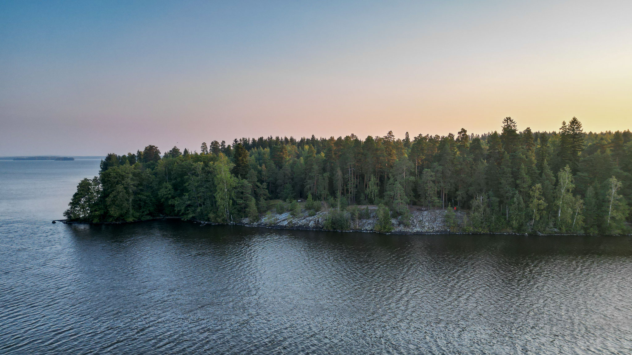 Niemen kärki, jonka rantaa reunustaa korkea kallio ja kallion päällä on metsää.