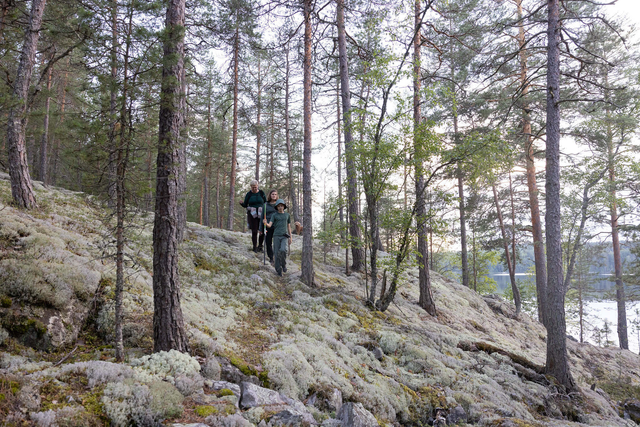 Lapsi ja kaksi aikuista kävelevät jäkälän peittämällä kalliolla.