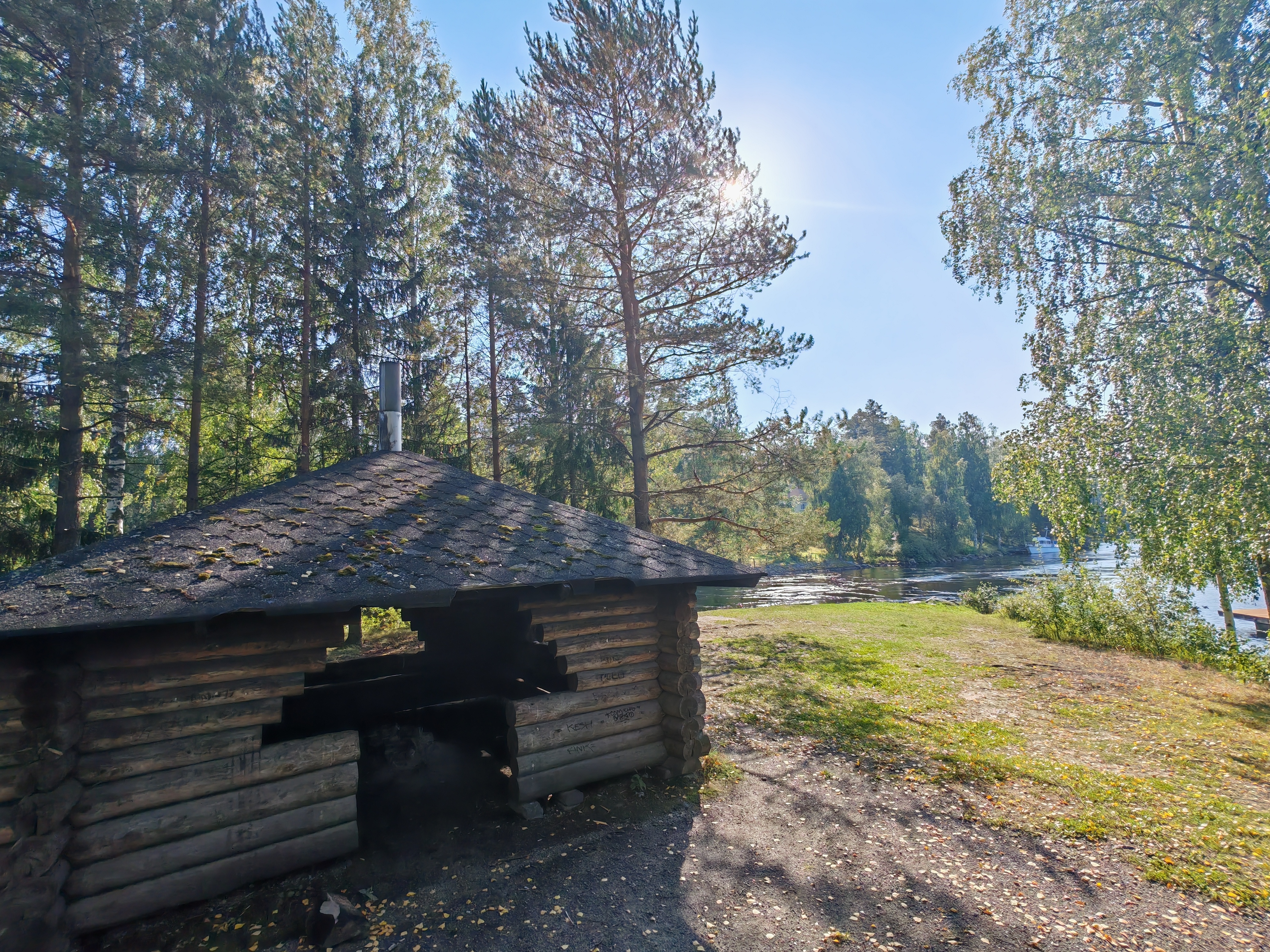 Kuvassa näkyy hirsinen laavu metsäisessä ympäristössä Vaajavirran rannalla. Laavu tarjoaa suojaisan paikan levähtää ja nauttia luonnon rauhasta.