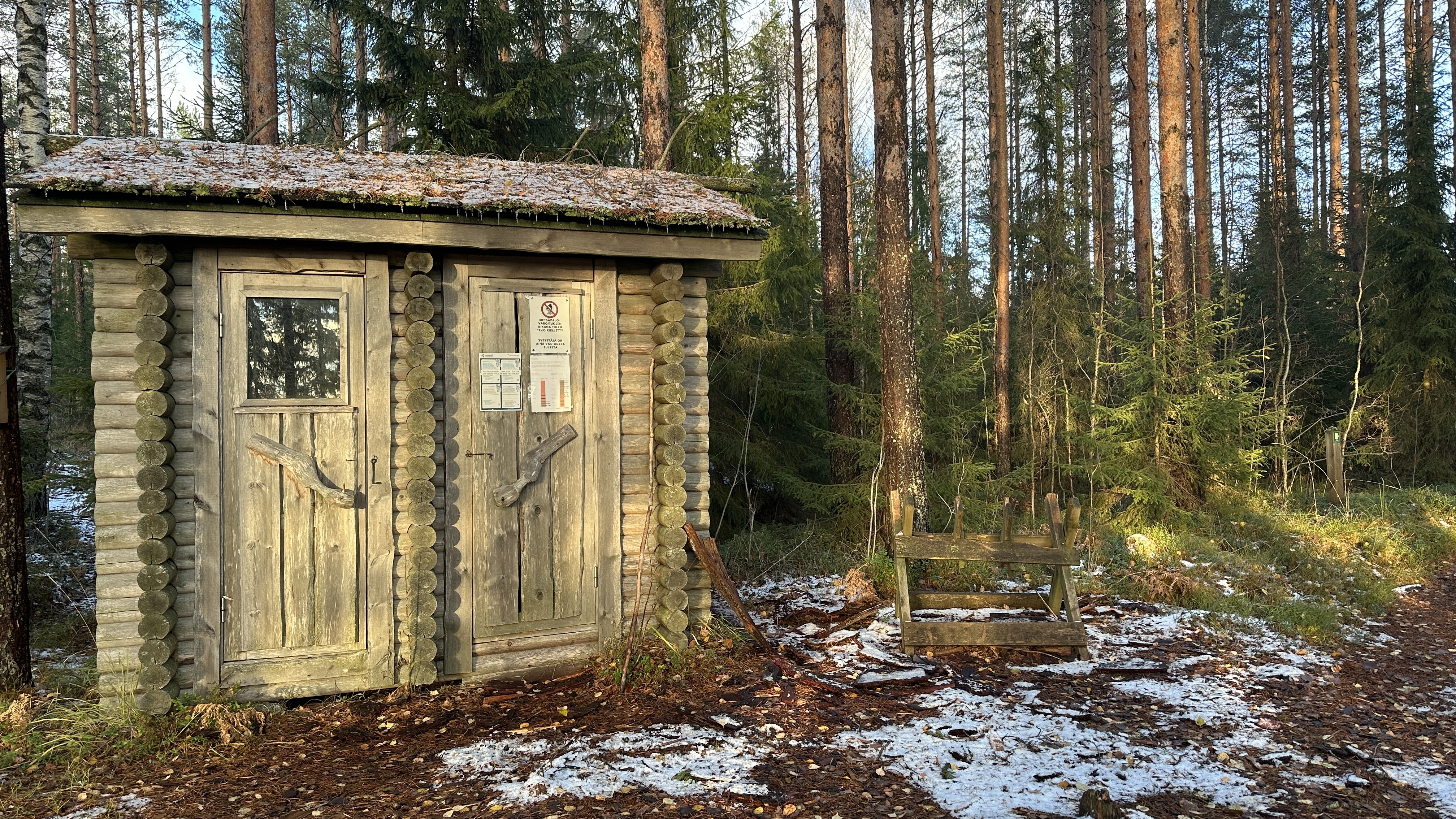 Puinen kaksiovinen rakennus metsässä.