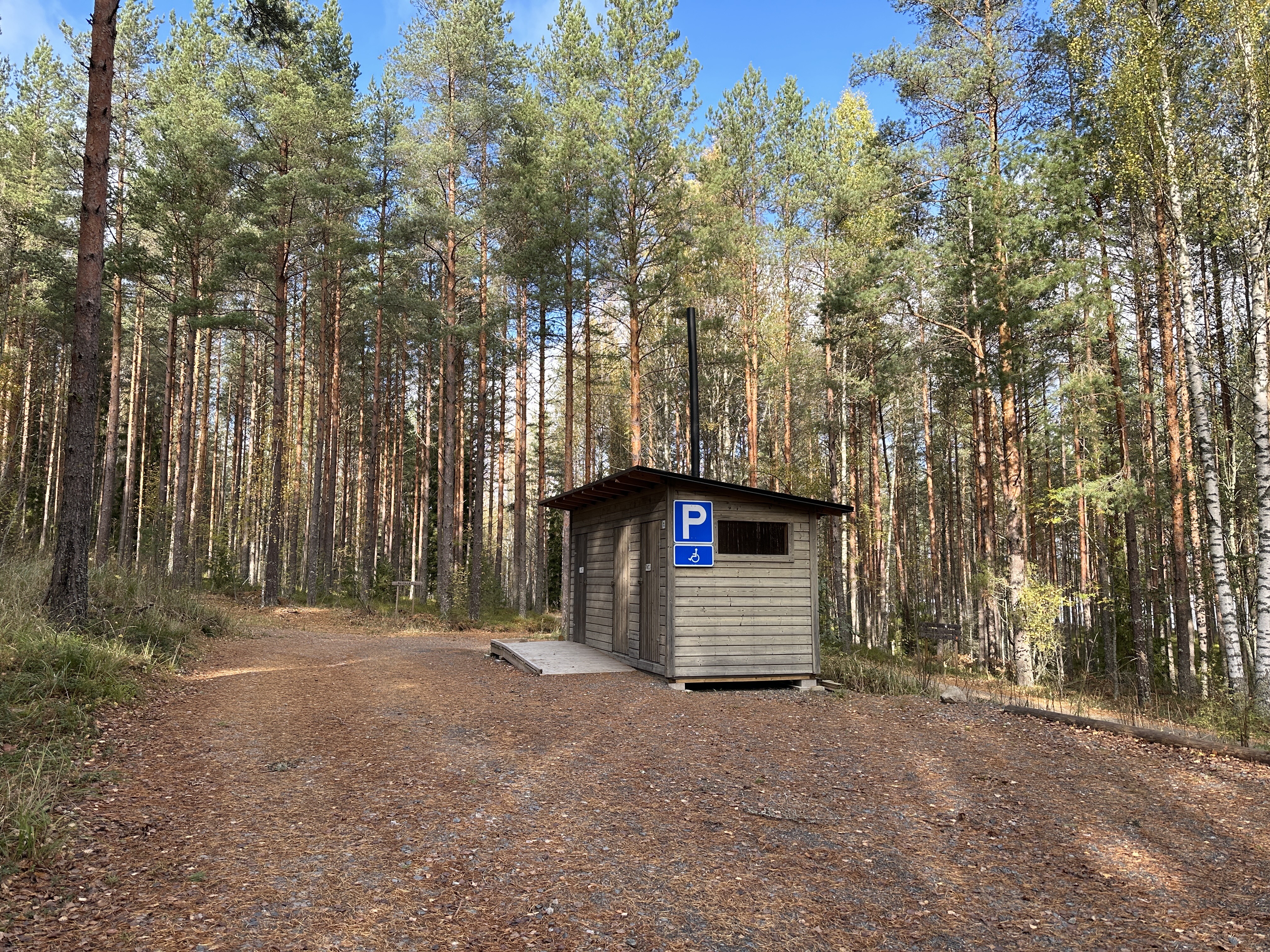 Hiekkakentällä metsän laidalla on puinen käymälä, johon on luiska.