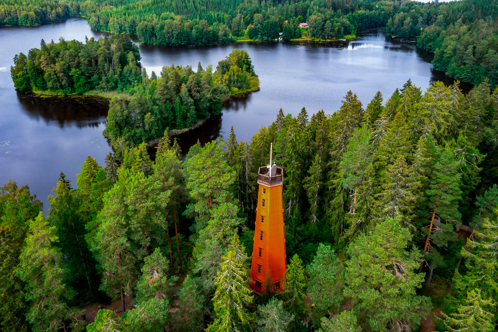 Oranssi torni metsän keskellä. Tornin alapuolella on järvi, jossa pieniä saaria.