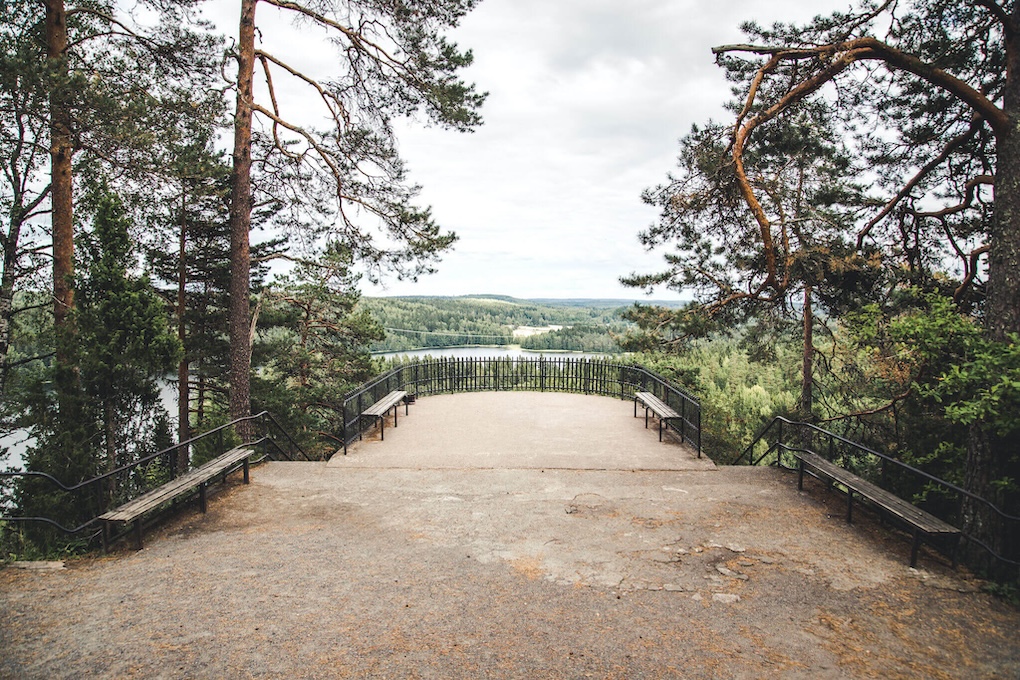 Näköalatasanteen edestä avautuu järvimaisema jonka takana on paljon metsää sekä harjuja.