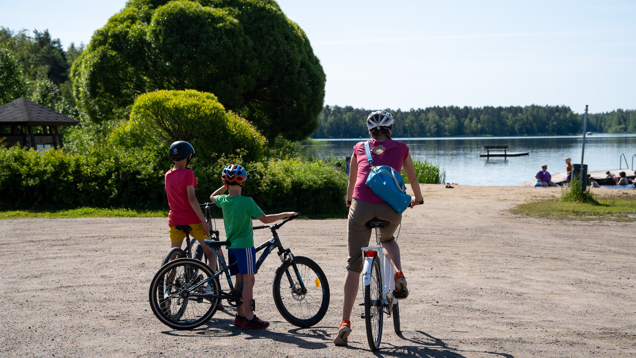 Aikuinen ja kaksi lasta ovat pysähtyneet pyörien kanssa katselemaan uimarantaa.