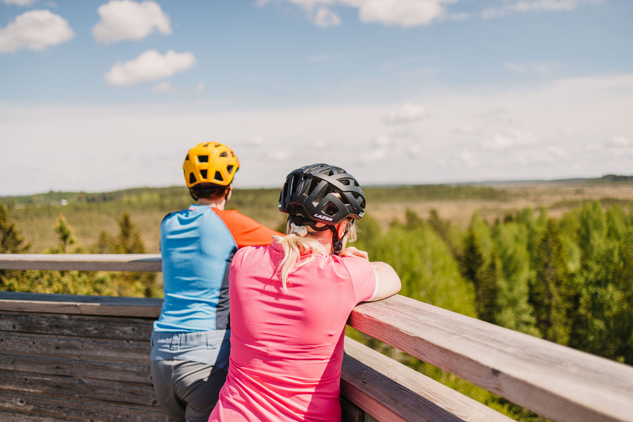 Two cyclists are looking at a vast bog from a nature tower.