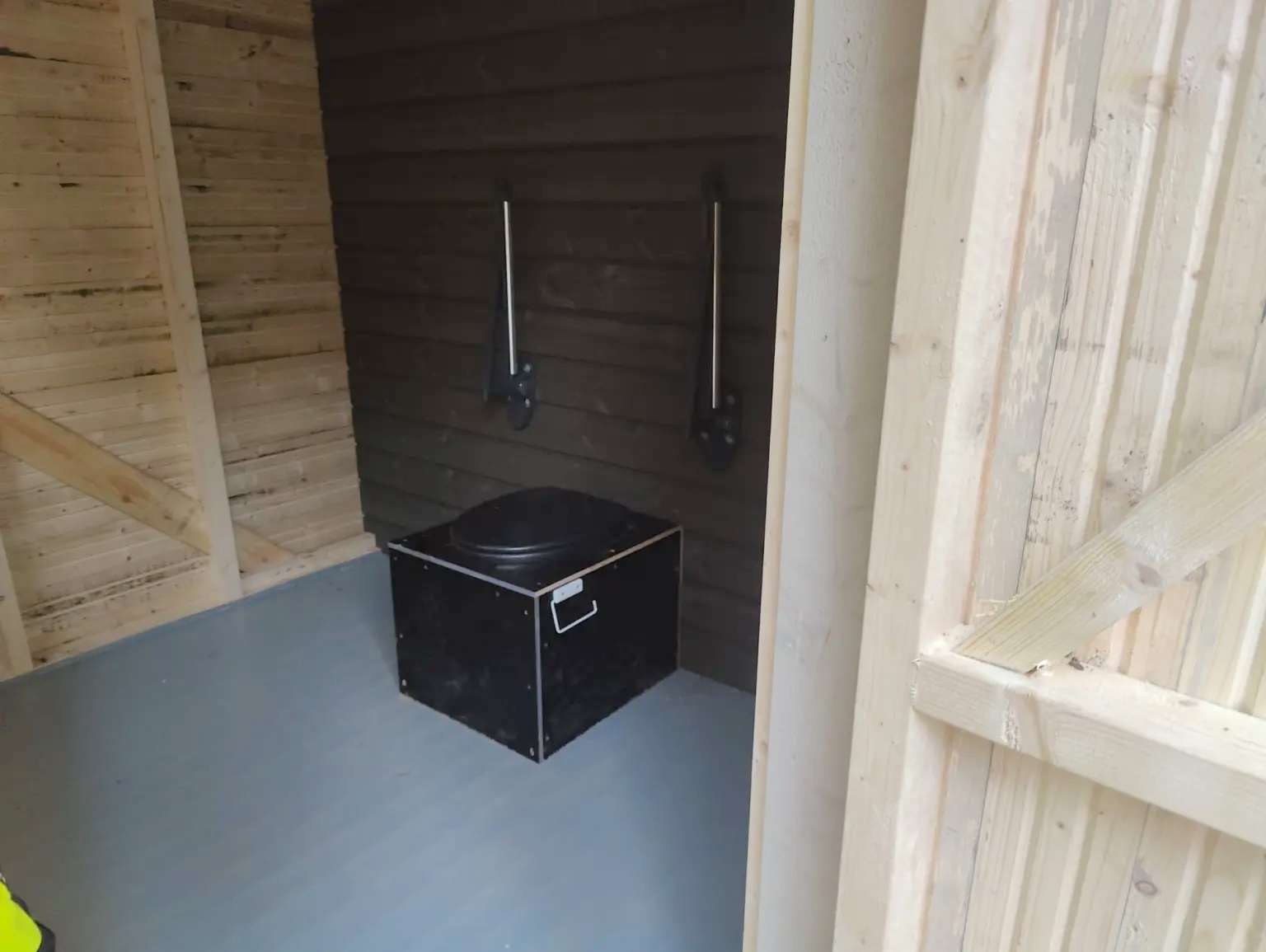 The toilet has fold-down support rails on both sides. The colour contrast between the toilet and the wall behind it is weak, which may make the toilet harder to distinguish.