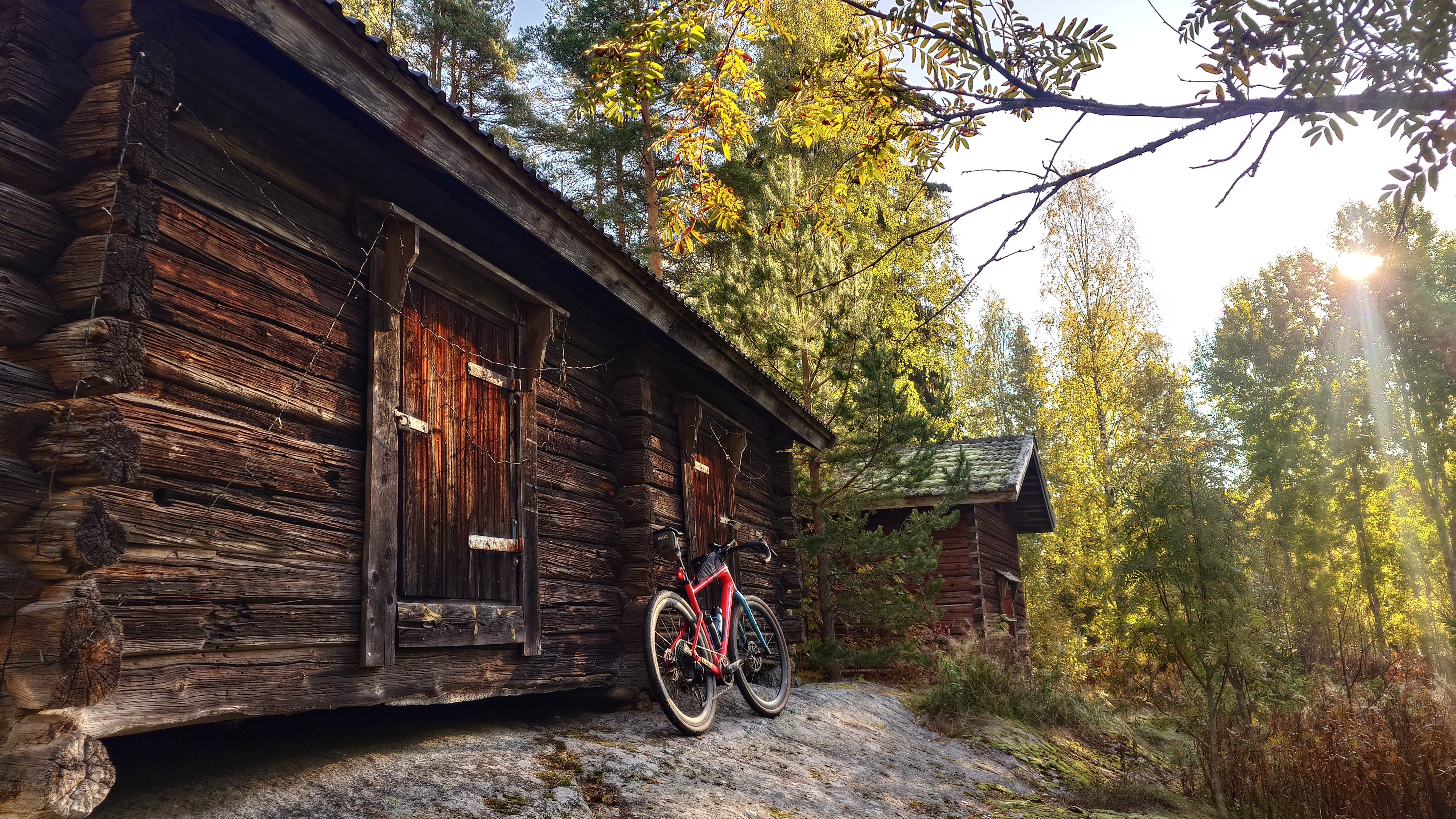 Kaksi hirsistä vanhaa aittaa, pyörä nojaa toista rakennusta vasten.