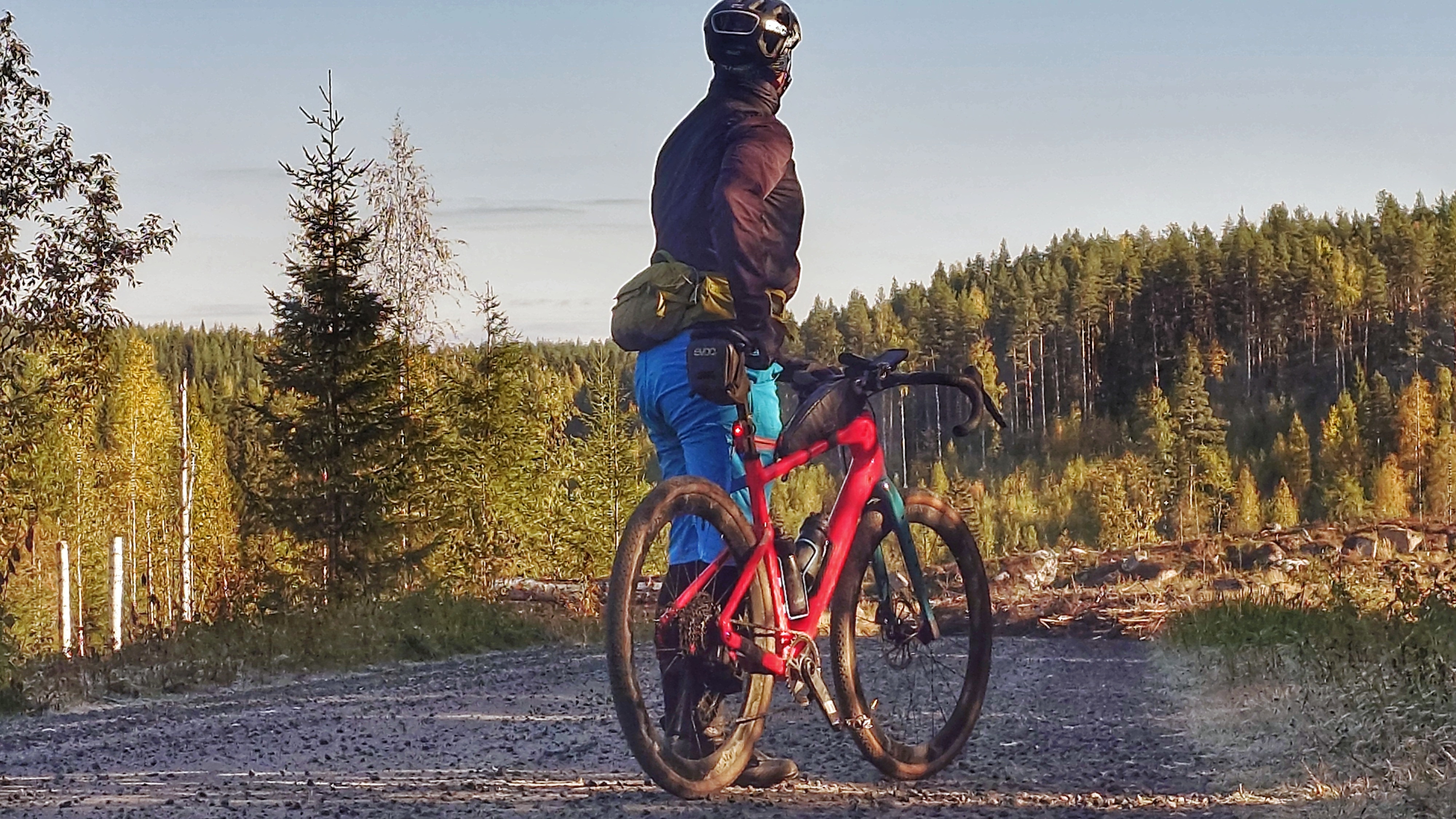 Pyöräilijä seisoo pyörän vieressä soratiellä katse kohti metsää.