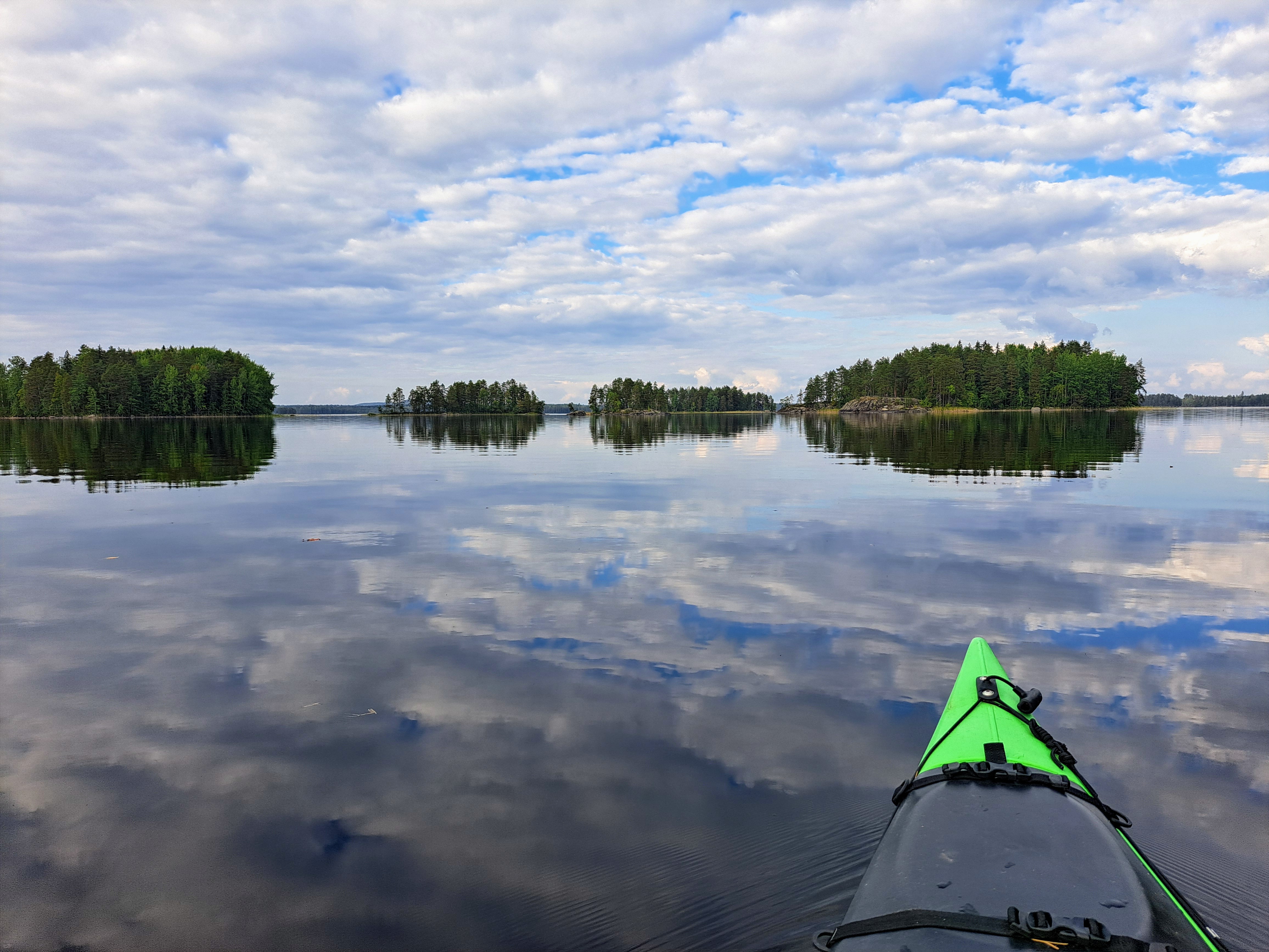 Kajakin keula näkyy etualalla, ja edessä siintävät Aittosalmen saaret tyynen veden ympäröiminä.