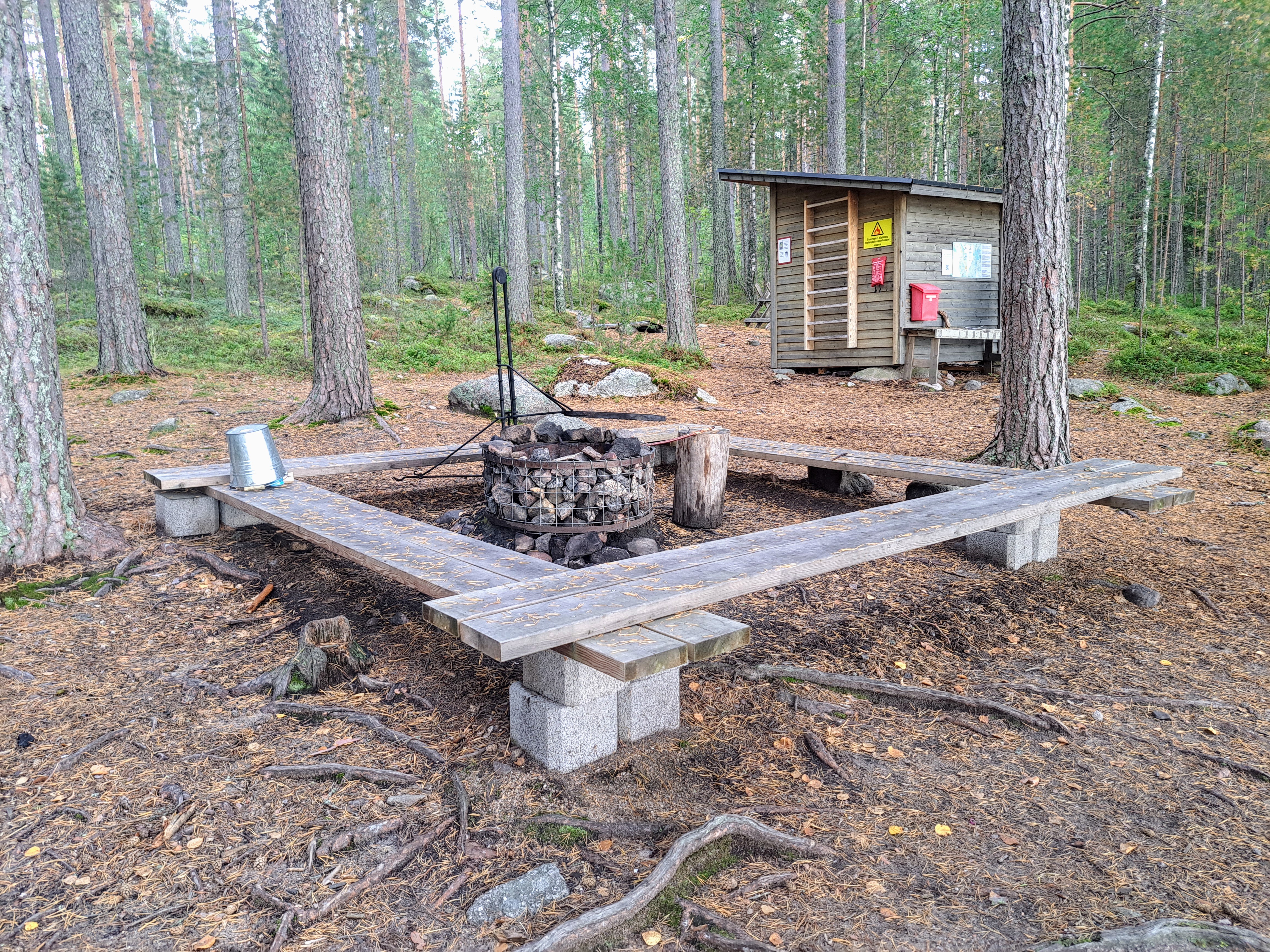 Tulipaikka maastossa, jossa kivinen tulipesä ja sen ympärillä puiset istumapaikat.