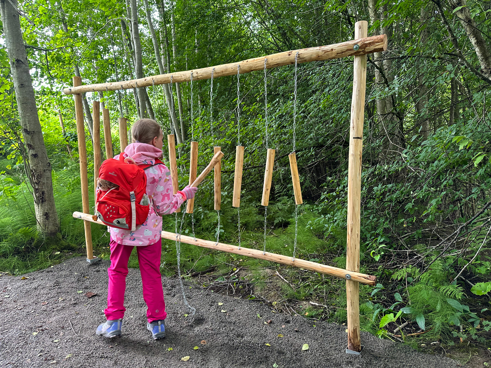 A child plays a large wooden xylophone in the woods along the trail.