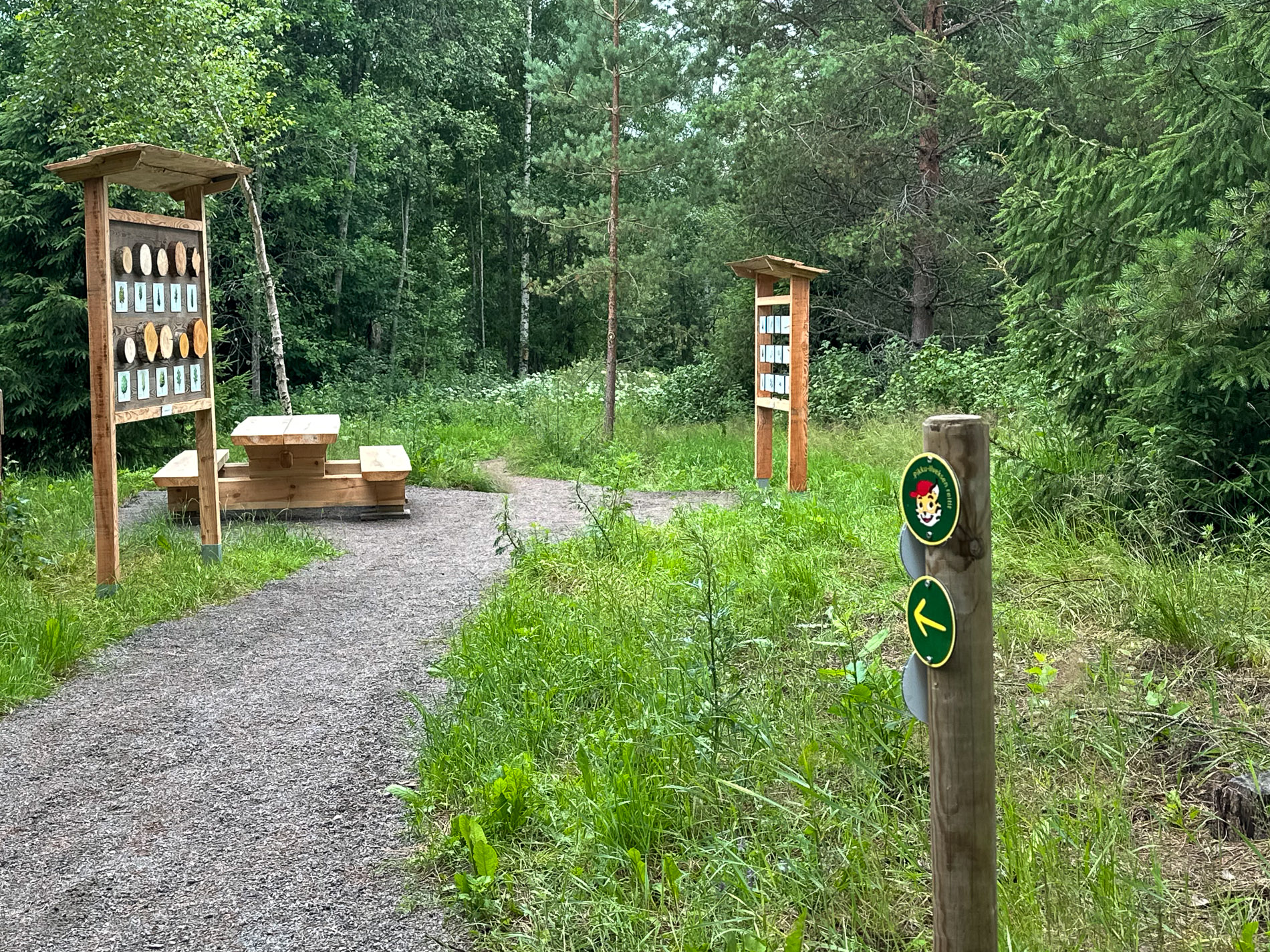 Signposts guide visitors along a gravel path to a clearing where there is a table and bench set and two information boards.